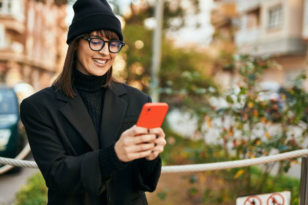 Joven mujer hispana sonriendo feliz usando smartphone en la ciudad. - Foto, Imagen