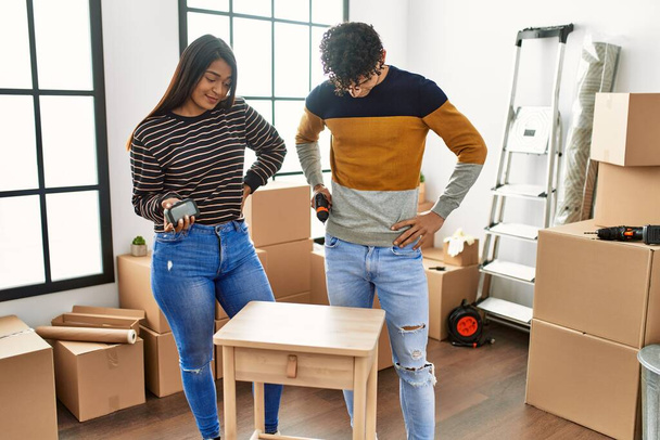 Joven pareja latina sonriendo feliz ensamblando muebles en un nuevo hogar. - Foto, imagen