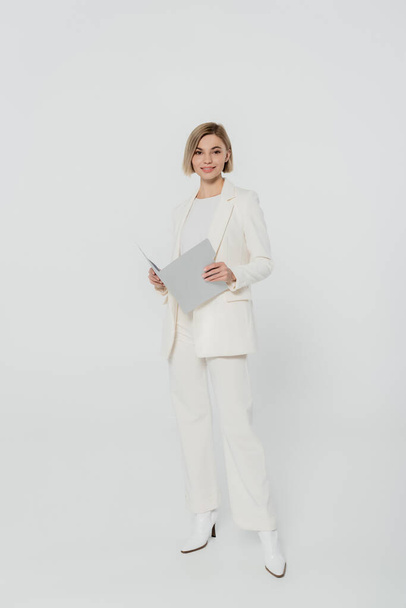 Full length of smiling businesswoman holding paper folder on grey background  - 写真・画像