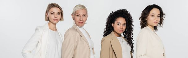 Multiethnic businesswomen in formal wear looking at camera isolated on grey, banner  - Photo, Image