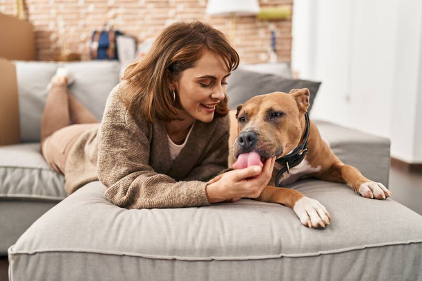 Jeune femme caucasienne souriante confiante couchée sur le canapé avec chien à la nouvelle maison - Photo, image