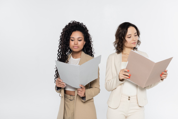 Multiethnic businesswomen in formal wear holding paper folders isolated on grey  - Fotoğraf, Görsel