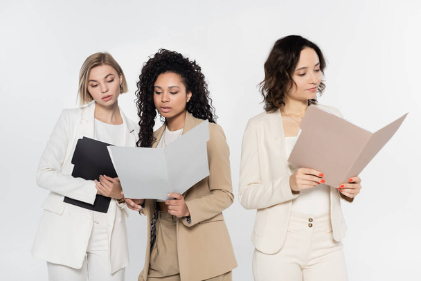 Interraciale zakenvrouwen met papieren mappen in de buurt van collega geïsoleerd op grijs  - Foto, afbeelding