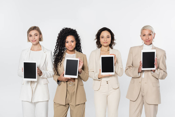 Multiethnische Geschäftsfrauen halten digitale Tablets mit leerem Bildschirm isoliert auf grau  - Foto, Bild