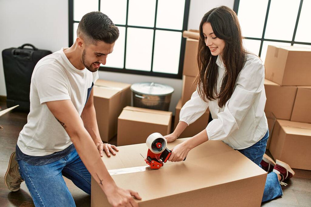 Young hispanic couple smiling happy packing cardboard box at new home. - Photo, Image