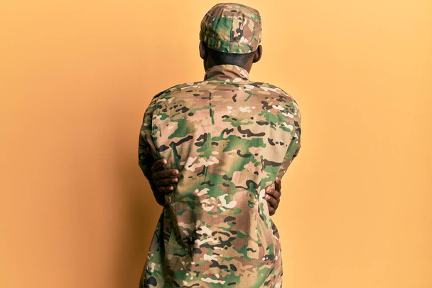 A fiatal afro-amerikai férfi katonai egyenruhát visel, és boldogan és pozitívan ölelkezik visszafelé. önszeretet és öngondoskodás  - Fotó, kép