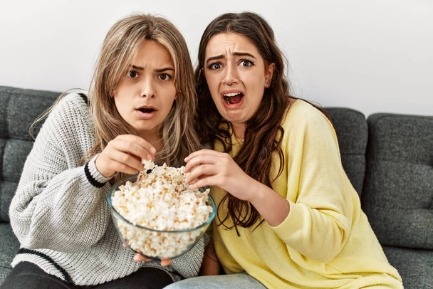 Junges Paar schaut verängstigt Horrorfilm und isst Popcorn zu Hause. - Foto, Bild