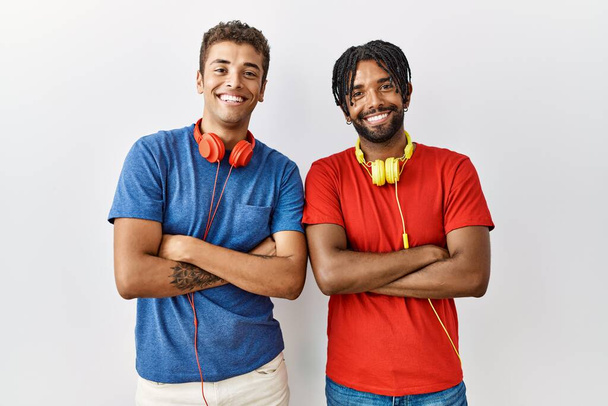 Young hispanic brothers standing over isolated background wearing headphones happy face smiling with crossed arms looking at the camera. positive person.  - Fotografie, Obrázek