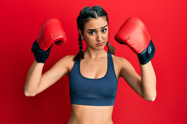 Young brunette girl using boxing gloves wearing braids skeptic and nervous, frowning upset because of problem. negative person.  - Foto, imagen