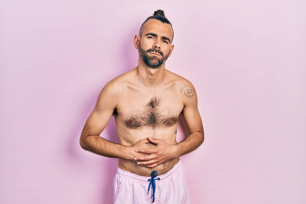 Fiatal spanyol férfi félmeztelenül fürdőruhában, kézzel a hasán, mert emésztési zavar, fájdalmas betegség rossz közérzet. fájdalom koncepció.  - Fotó, kép