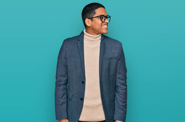 Young handsome hispanic man wearing business jacket and glasses looking away to side with smile on face, natural expression. laughing confident.  - Fotó, kép