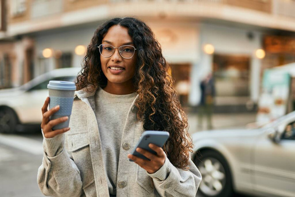 Jeune femme latine utilisant smartphone et boire du café à la ville. - Photo, image