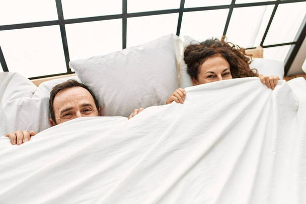 Середньовіччя іспаномовна пара покриває обличчя простирадлом, що лежить на ліжку вдома
. - Фото, зображення