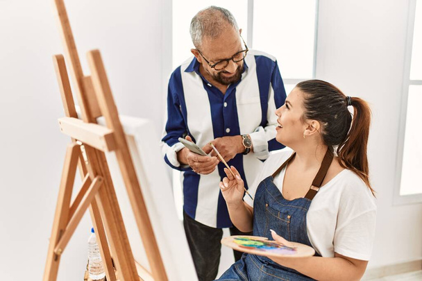 Profesor de pintura sénior hombre enseñando arte a la joven pintura sobre lienzo en el estudio de arte - Foto, Imagen