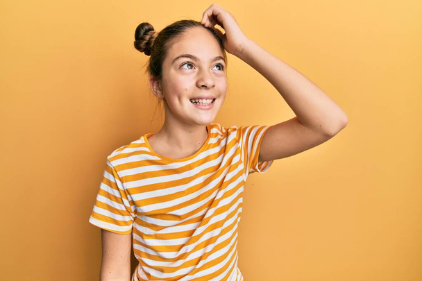 Όμορφη μελαχρινή κοριτσάκι φορώντας casual ριγέ t πουκάμισο χαμογελώντας αυτοπεποίθηση αγγίζοντας τα μαλλιά με το χέρι προς τα πάνω χειρονομία, θέτοντας ελκυστική και μοντέρνα  - Φωτογραφία, εικόνα