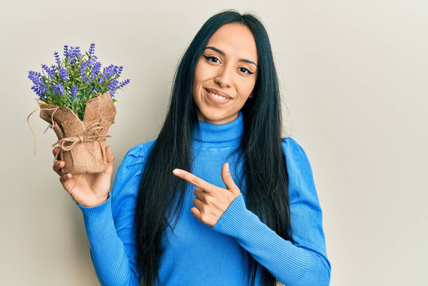 Young hispanic girl holding lavender plant smiling happy pointing with hand and finger  - Foto, Imagem