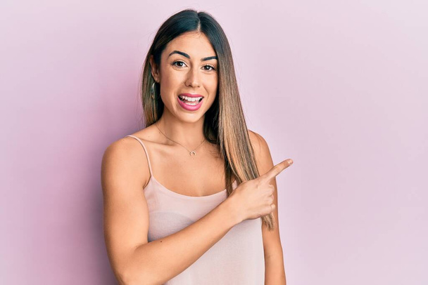 Young hispanic woman wearing casual sleeveless t shirt smiling cheerful pointing with hand and finger up to the side  - Photo, Image
