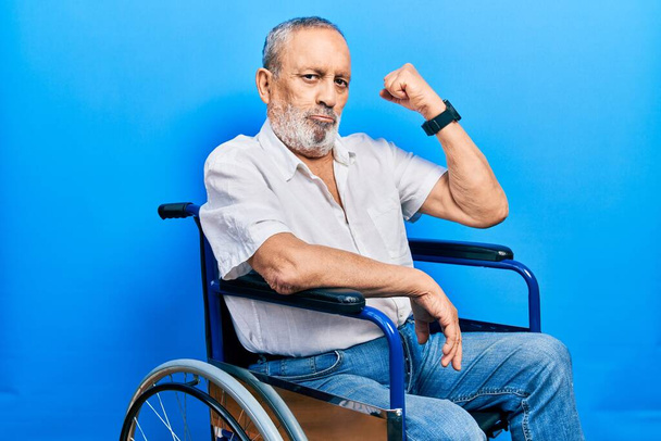Fešák starší muž s vousy sedí na invalidním vozíku silná osoba ukazující svaly paží, sebevědomý a hrdý na moc  - Fotografie, Obrázek