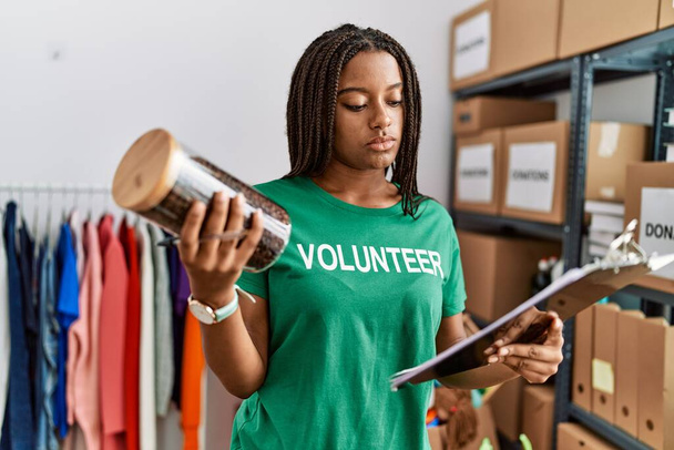 Genç Afro-Amerikan kadın gönüllü üniforması giyiyor. Yardım merkezinde elinde not panosu ve kahve kavanozu var. - Fotoğraf, Görsel