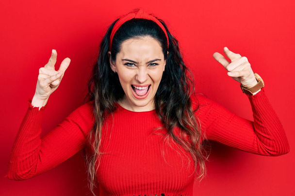 Jonge Latijns-Amerikaanse vrouw draagt casual kleding schreeuwen met gekke uitdrukking doen rock symbool met handen omhoog. Muziekster. zware muziek concept.  - Foto, afbeelding