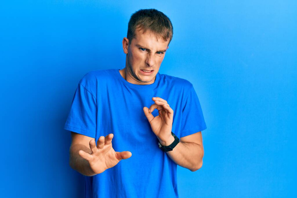 Νεαρός καυκάσιος άντρας που φοράει μπλε μπλουζάκι αηδιασμένη έκφραση, δυσαρεστημένος και φοβισμένος να κάνει γκριμάτσες επειδή η αντίδραση αποστροφής.  - Φωτογραφία, εικόνα