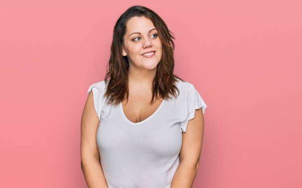 Молодая женщина плюс размер носить случайные белые футболки улыбаясь глядя в сторону и глядя в сторону, думая:.  - Фото, изображение