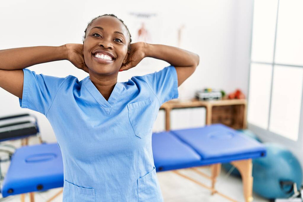 Чорна жінка з косами, що працюють у клініці відновлення болю, розслабляється та розтягується, руки та руки позаду голови та шиї посміхаються щасливо
  - Фото, зображення