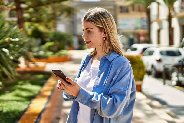 Young blonde girl smiling happy using smartphone at the city. - Foto, Bild