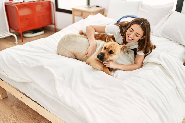 Молода іспаномовна жінка грає з собаками, сидячи в ліжку в спальні
 - Фото, зображення