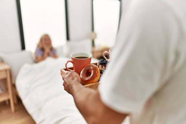 Hombre sorprendiendo a su novia con el desayuno en la cama en casa. - Foto, imagen