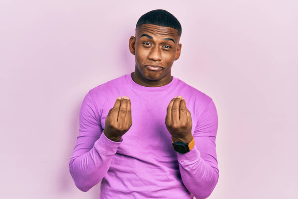 Young black man wearing casual pink sweater doing money gesture with hands, asking for salary payment, millionaire business  - Foto, Bild