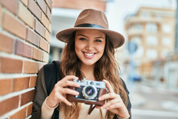 Jovem turista hispânica sorrindo feliz usando a câmera vintage na cidade. - Foto, Imagem