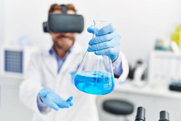 Keski-ikä latino mies yllään tiedemies yhtenäinen käyttäen vr lasit tilalla koeputki laboratoriossa - Valokuva, kuva
