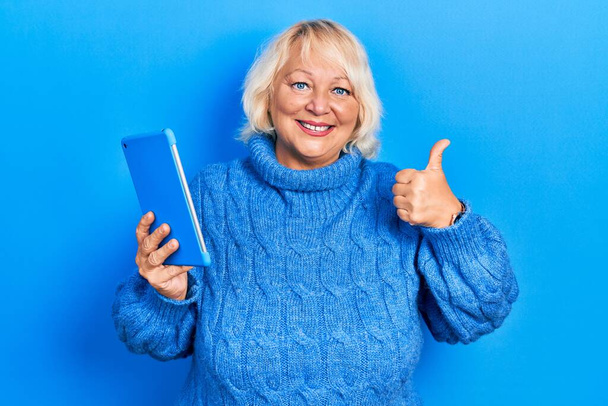 Blondynka w średnim wieku za pomocą touchpad urządzenie uśmiecha szczęśliwy i pozytywny, kciuk do góry robi doskonałe i znak aprobaty  - Zdjęcie, obraz