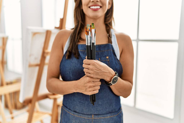 Νεαρή Ισπανίδα καλλιτέχνιδα χαμογελά χαρούμενη ζωγραφιά στο στούντιο τέχνης. - Φωτογραφία, εικόνα