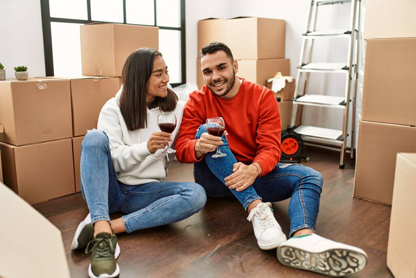Junges lateinisches Paar lächelt glücklich und stößt mit Rotwein auf neues Zuhause an - Foto, Bild
