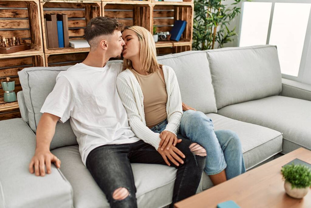 Nuori valkoihoinen pari suudella ja halata istuu sohvalla kotona. - Valokuva, kuva
