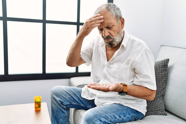 Starszy siwowłosy mężczyzna bierze pigułki na ból głowy w domu - Zdjęcie, obraz