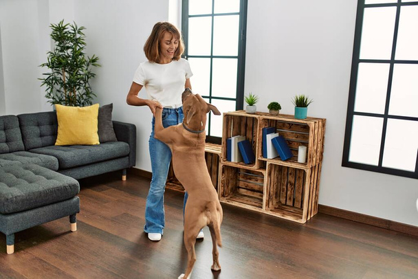 Beyaz bir kadın gülümseyerek evde köpekle dans ediyor. - Fotoğraf, Görsel