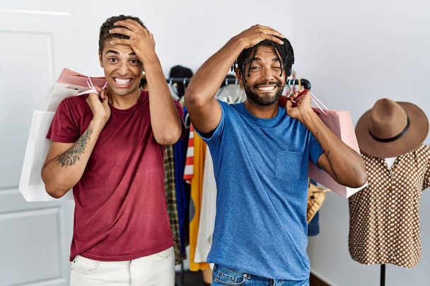 Jonge Latijns-Amerikaanse mannen houden boodschappentassen in de mode boetiek gestrest en gefrustreerd met de hand op het hoofd, verrast en boos gezicht  - Foto, afbeelding
