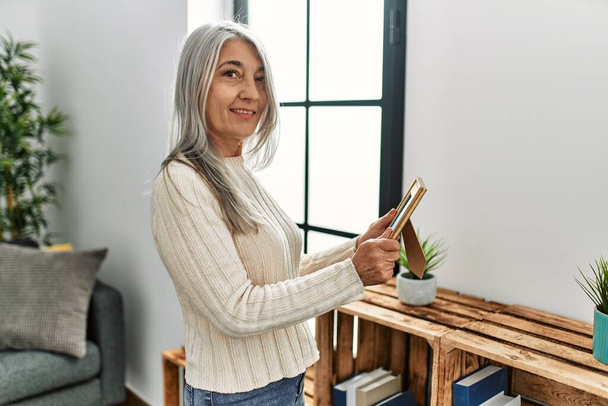 Moyen âge femme aux cheveux gris souriant confiant regardant photo à la maison - Photo, image