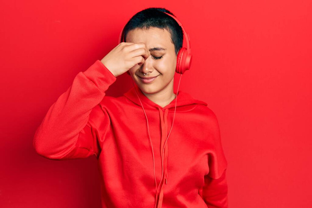 Beautiful hispanic woman with short hair listening to music using headphones tired rubbing nose and eyes feeling fatigue and headache. stress and frustration concept.  - 写真・画像