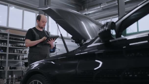 Auto monteur die met auto kenmerkend hulpmiddel in een reparatiewerkplaats werkt. Car Service Manager of Mechanic Gebruikt een Tabletcomputer met een Futuristische Interactieve Diagnostieksoftware. - Video