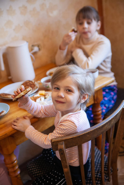 Petite fille avec sœur aînée à la table du petit déjeuner mangeant des crêpes.  - Photo, image