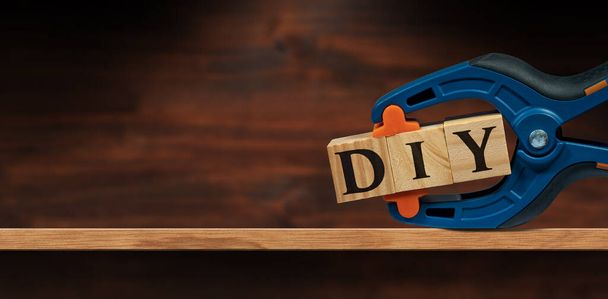 Close-up of a spring plastic clamp and text Diy (do it yourself), made of wooden blocks, above a wooden shelf or workbench with copy space. - Photo, Image
