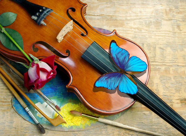 Geige, Künstlerpalette, Pinsel, rote Rose und blauer Morpho-Schmetterling. Kunstkonzept. - Foto, Bild