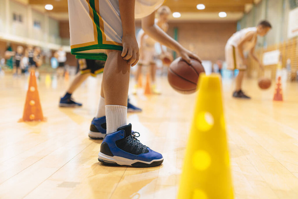 若いバスケットボール選手はトレーニングセッションでボールをバウンス。子供のためのバスケットボールスクール。バスケットボールのスポーツウェアの子供たちはスキルを向上させます - 写真・画像