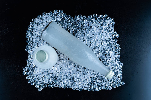 Una botella blanca con un refresco sobre hielo sobre un fondo negro.  - Foto, Imagen