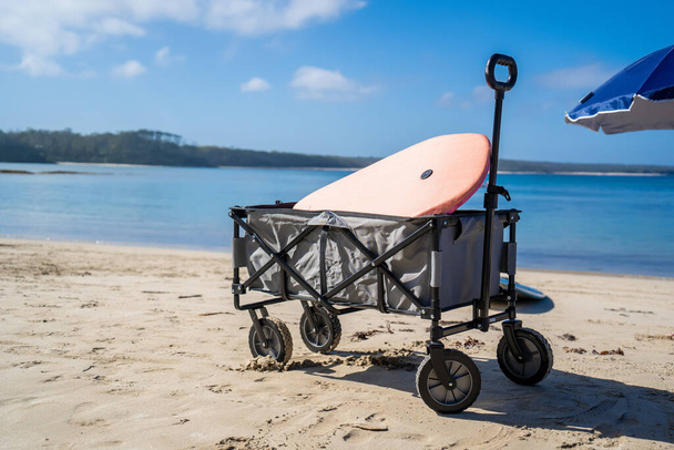 Venkovní plážový vozík vůz a plážový deštník na písečné pláži v blízkosti oceánu. Koncept rodinné dovolené - Fotografie, Obrázek