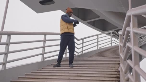 Pełnowymiarowe spowolnienie boksera afro-amerykańskiego w ciepłej odzieży aktywnej rozgrzewającej się na schodach na zewnątrz podczas treningu bokserskiego - Materiał filmowy, wideo